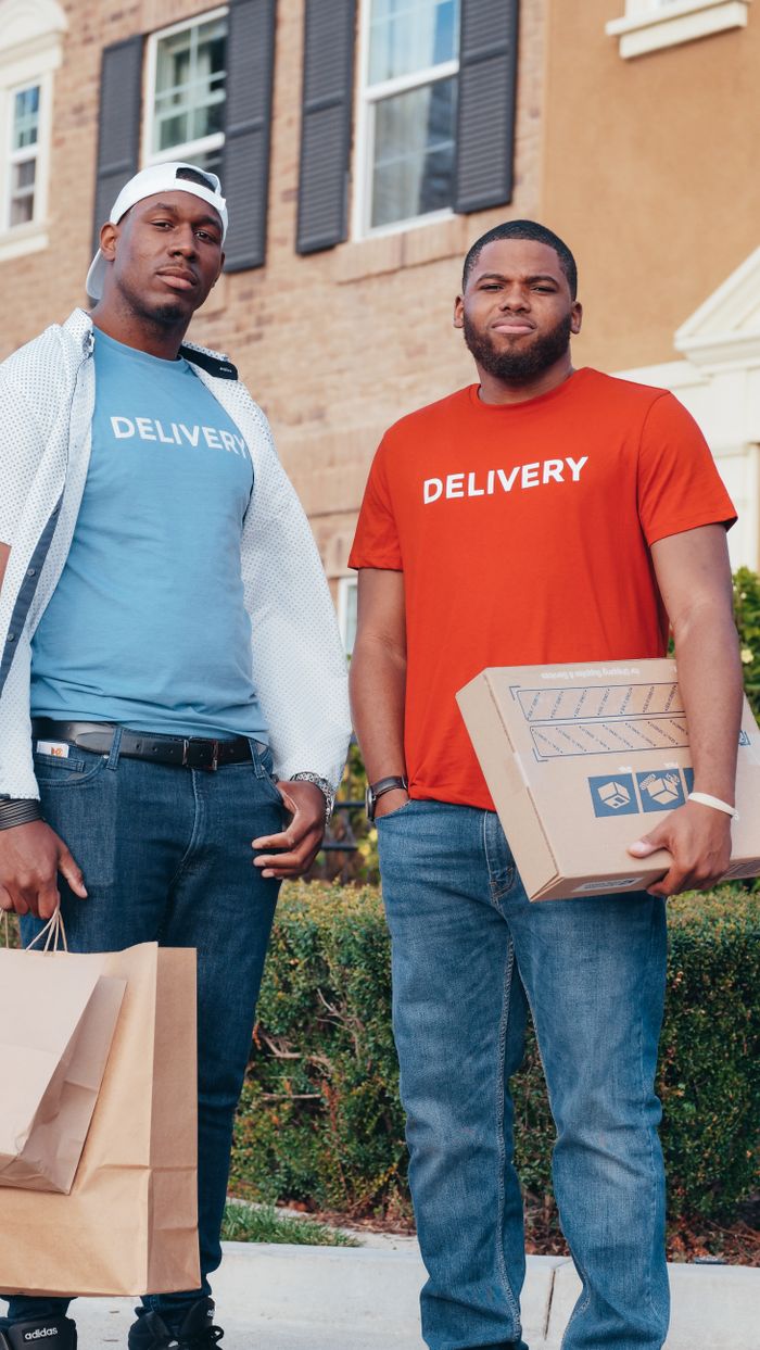 Two delivery workers holding packages outside a residential building, showcasing modern commerce.